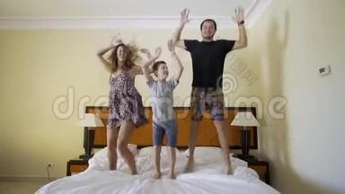幸福的一家人在床上跳。 幸福的家庭观念。 爸爸，妈妈和小男孩跳在床上