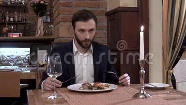 一个留着胡子的人坐在餐厅的桌子旁。 吃肉菜，享受美食。