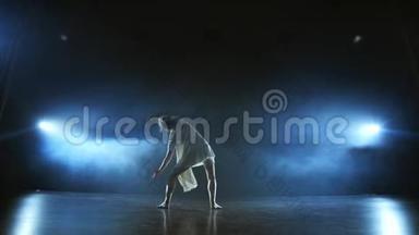 一位穿着白色连衣裙的年轻舞者在舞台上跳舞，舞台上的烟雾弥漫在聚光灯下。