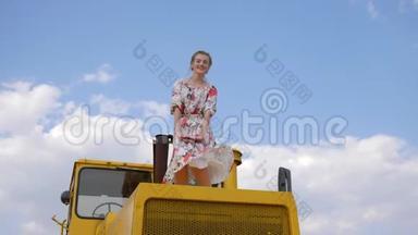 年轻女子穿着礼服，挥舞着手，跳上拖拉机的引擎盖，背景天空白云