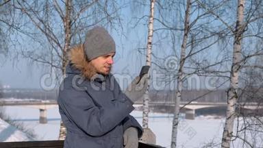 穿着蓝色羽绒服的人，带着毛皮罩，在冬季公园里用手机进行视频聊天和微笑。
