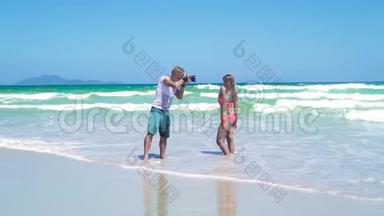 男子摄影师拍摄年轻女子比基尼在海边摆姿势。 年轻的摄影师