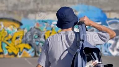 一个带背包的成年男子朝一面涂鸦墙的后景