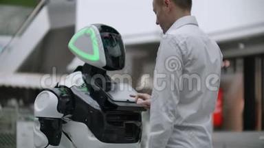 一个穿衬衫的男人和一个白色机器人交流，他<strong>问问</strong>题，用手指按屏幕。