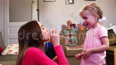 一位母亲给她的小女孩吹了一个肥皂泡，她正在做滑稽的脸。 婴儿缓慢地拍拍手。