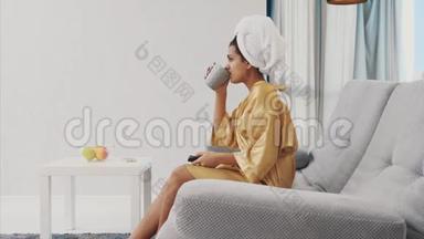 年轻<strong>女子</strong>穿着晨衣，头上戴着毛巾。 <strong>坐在沙发上</strong>，手里拿着一个黑色的