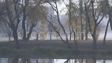 早晨，一位年轻女子在浓雾中沿着河岸在一个城市公园慢跑。 任何天气的健康生活方式