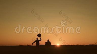 两个徒步旅行者在日落时跑、跳、跳、扔背包的剪影。 慢动作。 概念旅行