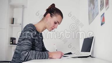 美丽<strong>的</strong>年轻女子坐在桌子旁，用钢笔写<strong>一封信</strong>。 打开桌上<strong>的</strong>笔记本电脑。 女商人