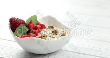 那人`手把一盘莫斯利放在桌子上。 健康的早餐。 燕麦片与草莓和坚果放入白碗