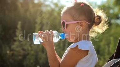 戴太阳镜的<strong>女孩子</strong>从瓶子里喝水。 阳光明媚的一天，儿童肖像特写