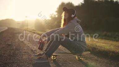 一个女孩坐在路边的素描板上听耳机音乐的肖像。 青少年