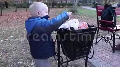 一个小男孩在街上的垃圾桶里扔垃圾。 废物管理和环境保护的理念.. 适当的做法