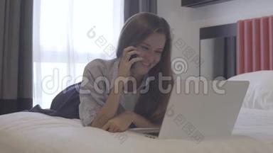 在线<strong>商务</strong>。 女人在笔记本电脑上工作时<strong>打电话</strong>，躺在床上。