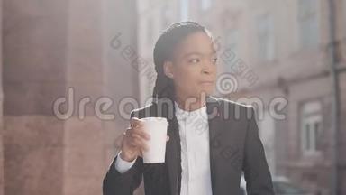 一个严肃的非洲裔美国女商人穿着西装，在城市里<strong>走来走</strong>去，喝着咖啡的肖像。 概念