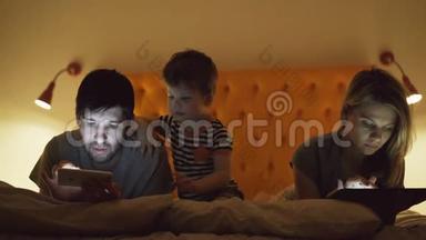 幸福的家庭，小儿子躺在床上，用平板电脑和智能手机看电影和卡通。