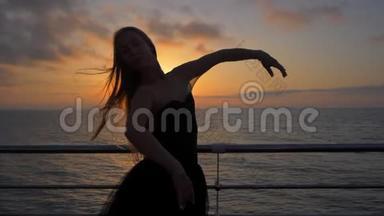 下面的动作。 美丽的芭蕾舞演员表演皮鲁埃特。 穿着黑色芭蕾舞裙的金发女子在海堤上或