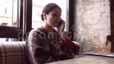 女人在智能手机上使用应用程序，在咖啡馆里喝咖啡，微笑着在手机上发短信。 美丽的多元文化青年
