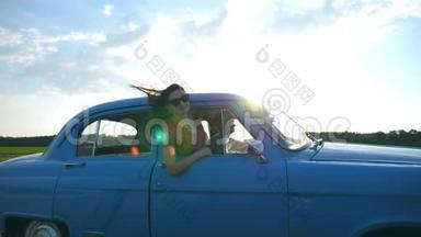 迷人的女孩戴着太阳镜，斜靠在老式车窗外，享受<strong>旅行</strong>。 年轻夫妇乘<strong>坐</strong>复古车<strong>旅行</strong>