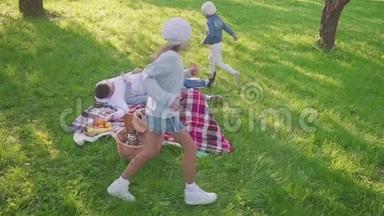 父母躺在草地上，他们的两个女儿在公园里玩得很开心，也有跑步的背景。 家庭度假景观。