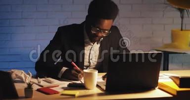 年轻的黑人商人带着笔记本电脑和文件在夜间办公室工作。 他在文件上签字。 商务