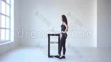 瘦骨嶙峋的女教练正在白色的独立工作室里靠在<strong>椅子</strong>上踢腿。 <strong>侧面</strong>全景