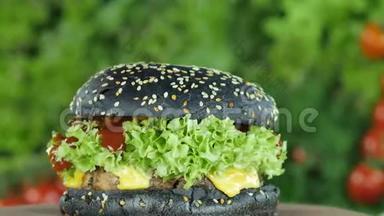 芝士汉堡或汉堡，上面有小牛肉、黄瓜和一个黑色的面包，模糊的<strong>生菜叶</strong>和蔬菜