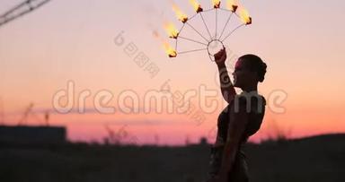 火舞者对抗日落。 在舞蹈表演中，一个年轻的女人用她的火箍在夕阳下摆姿势。