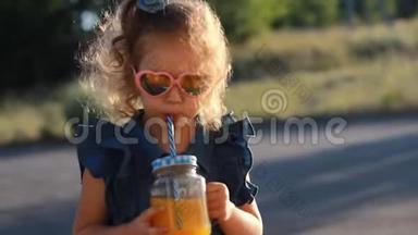 戴太阳镜的小女孩在夏日的夕阳下喝冰沙。 关门