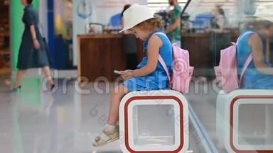在机场候机楼里坐在等候室里的儿童游客在等待他们的时候玩手机