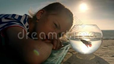 漂亮的小女孩躺在海滩上，在室外水族馆看鱼。 概念假期