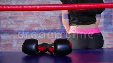 运动装女子运动员身材苗条，前台红黑拳击手套戴在拳击台上