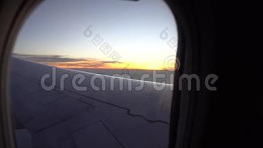 从飞机窗口日落。 观橙色的太阳，飞机的翅膀，黑暗的天空和云彩。