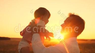 爸爸手中的漂亮女儿在灿烂的夕阳下微笑。 快乐爸爸在一个夏天的晚上在公园里和宝宝玩。