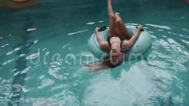 美丽的金发女人，穿着黑色泳衣的完美身材，正在游<strong>泳池</strong>里的<strong>充气</strong>橡胶圈上游泳。 4k.