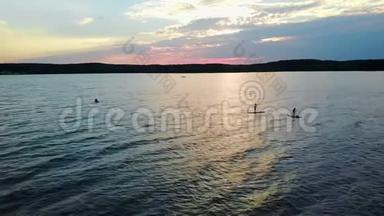 4K. 日落时SUP湖冲浪。 朋友们在太阳升起的时候在SUP板上航行。 空中景观