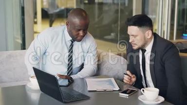 两位多民族的商业同事穿着正式服装，坐在桌子旁，一边看着财务图表，一边讨论财务图表