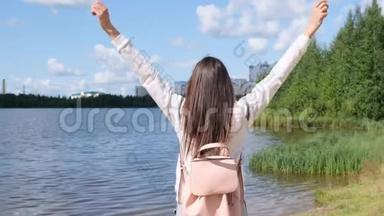 张开双手的女孩。 自然自由。 一个女孩站在那里享受美丽的阳光。 一个女孩站在水边