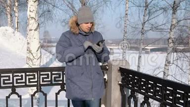 在冬<strong>季</strong>公园里，穿着蓝色夹克，带着毛皮罩的人用手戴手套擦拭<strong>手机</strong>屏幕。