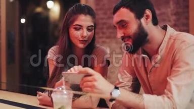快乐的年轻夫妇，有智能手机聊天和饮料坐在酒吧。 使用手机智能手机的朋友