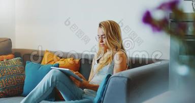 高质量的4k12位镜头美丽的女孩使用平板电脑坐<strong>在家</strong>里的沙发上。 女人<strong>上网</strong>，社交