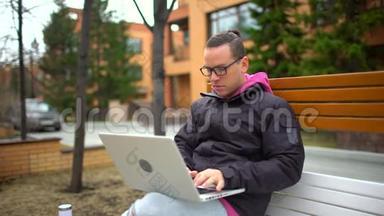 在笔记本电脑上工作的人，微笑着，在户外，多利射击。 西班牙裔男子戴眼镜工作与笔记本电脑。 一幅肖像画