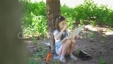 夏天，白种人的小女孩坐在树下用画笔画画
