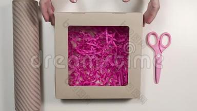 打开带粉色纸的节日盒包装礼物，桌上放有剪刀的包装纸，DIY包装