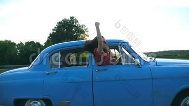 迷人的女孩戴着太阳镜，斜靠在老式车窗外，享受旅行。 年轻夫妇乘坐复古车旅行