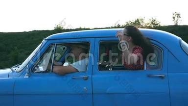 迷人的女孩戴着太阳镜，斜靠在老式车窗外，享受旅行。 年轻夫妇乘坐复古车旅行