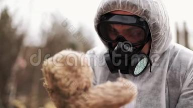 一个穿着生物危险服和防毒面具的男人怀里抱着一个玩具
