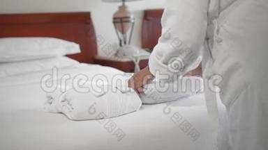 一位未被认出的成年高级妇女把一条<strong>白色</strong>毛巾放在酒店房间的床上，旁边是一件<strong>白色浴袍</strong>。 慢动作