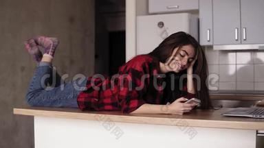 一个年轻女孩在她的厨房桌面上躺着，发短信给某人时微笑和大笑的慢镜头。