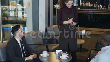 两位穿着正式服装的多民族商人在午餐休息期间坐在时尚的咖啡馆里微笑着点餐